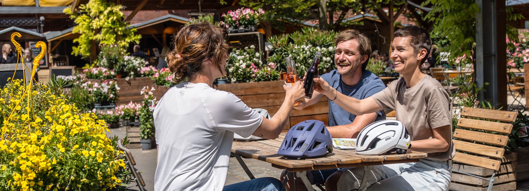 drei Personen am Tisch stossen mit Getraenken an